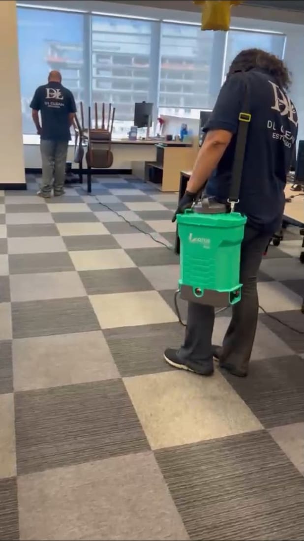 Dois técnicos do Grupo DL Clean uniformizados aplicando produto no carpete de um escritório