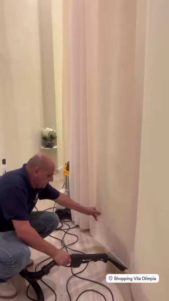 Técnico do Grupo DL Clean limpando uma cortina clara ainda pendurada no trilho
